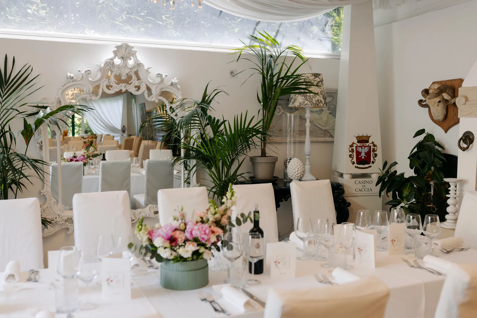 Una sala allestita con fiori, specchi e tavole bianche per un ricevimento